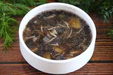 Yaban mantar çorbası, siyah et suyu ve ahşap bir masanın üzerinde yeşil bir arka planda mercangiller.
