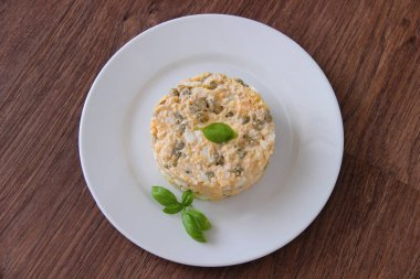 Morina ciğeri, bezelye, yumurta ve peynirli ev yapımı salata, mayonez ve fesleğenle süslenmiş, beyaz tabakta ve ahşap arka planda, üst manzara