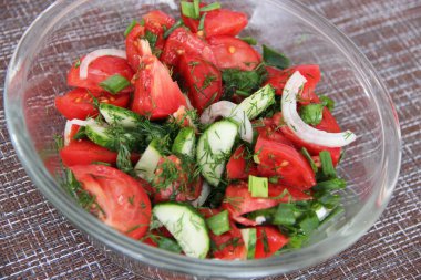 Şeffaf bir fincanda taze salatalık ve soğanlı domates ve ottan oluşan ev yapımı salata.