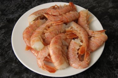 Kabuklu büyük karidesler, kafasız beyaz tabakta ve siyah arka planda, üst görünümde.