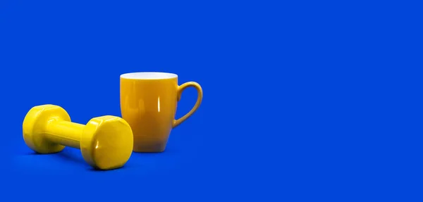 Home workout self isolation gym online sport concept. A yellow dumbbell, tea cup on contrast vibrant blue background with free copy space for text. Website banner, social media profile header, card