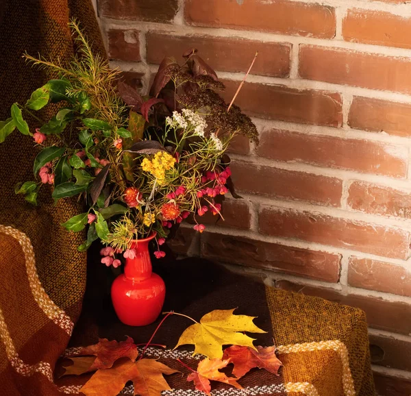 Autumn fall branches leaves flower and berry yellow red bouquet in a tiny orange vase in front of brown plaid drapery and brick wall background. A photo with free blank copy space for text — Stock Photo, Image