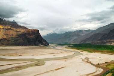 Pakistan 'da bahar mevsiminde dağları olan güzel bir çöl manzarası. Gri bulutlar, vadide geniş çöl, büyük tepeler. Güzel Asya doğası.