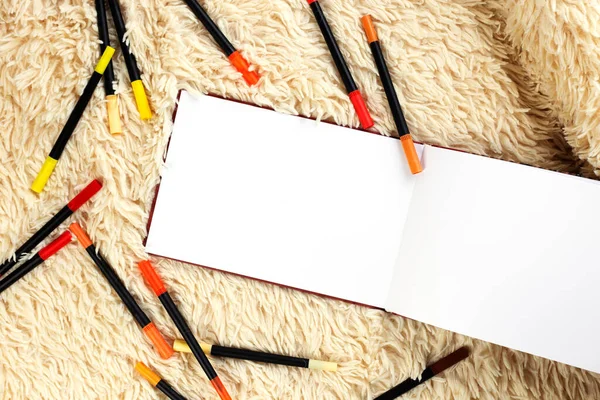 Beautiful various colorful sketch markers for coloring and drawing tools and white sketchbook on yellow fluffy background. Top view, copy space
