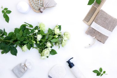 Spa aksesuarları ve beyaz güllü masaj fırçaları. Çiçeklerle sıfır atık düz konsept. Tahta fırça, sünger, tarak ve doğal malzemeden yapılmış el bezi. Üst görünüm