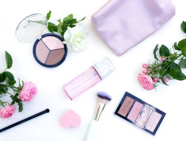 Beyaz arka planda çeşitli kozmetik ürünleri ve çiçeklerle düz bir yerleşim