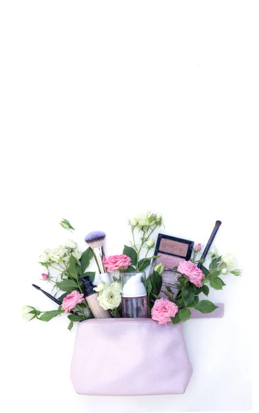 Vários produtos cosméticos e flores em um saco rosa no fundo branco — Fotografia de Stock