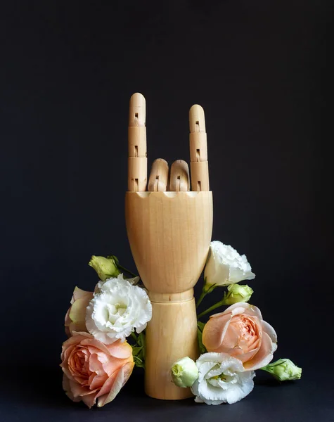 Wooden hand making Devils horns with flowers on black background