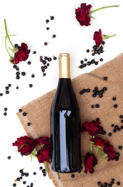 Sangria için malzemeler. Bir şişe şarap, siyah frenk üzümü, beyaz arka planda kırmızı güller ve çuval bezi. Böğürtlenli ev yapımı şarap konsepti. Düz yatış, üst görünüm.