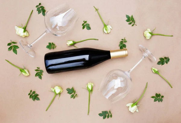 Flat lay. Minimal style. Minimalist trend. Empty wineglasses and a bottle with fresh white roses and green leaves on beige pastel background. Wine shop or wine tasting concept. Homemade wine. Top view