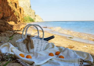 Deniz kenarındaki kırsal giysinin üzerinde romantik piknik seti. Beyaz piknik sepeti, bir şişe şarap, bir çift bardak ve biraz kayısı. Plajda yaz pikniği