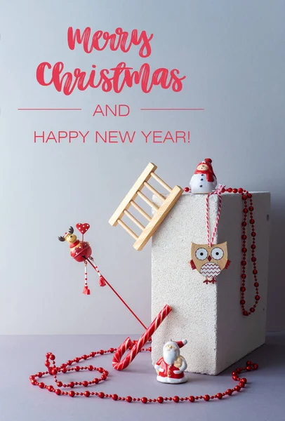 Kırmızı renk dekorasyonu dengeli modern minimalist noel kompozisyonu. Geyik, kardan adam, Noel Baba, baykuş ve noel boncukları. Gri arkaplanı olan alternatif tebrik kartı