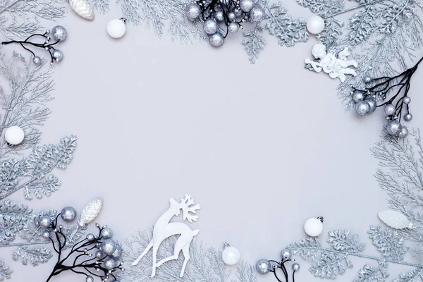 Noel kompozisyonu. Gri arkaplanda beyaz ve gümüş süslemelerden yapılmış çerçeve. Parlak toplar, geyik, melek. Noel, kış, metal yeni yıl konsepti. Tek renkli düz zemin, üst görünüm, boşluğu kopyala