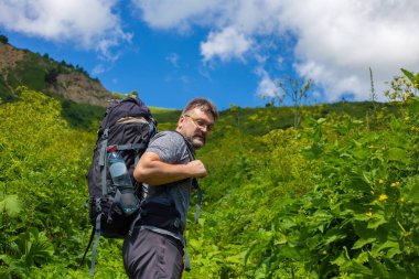 Sırt çantalı gezgin dışarıda dinleniyor ve arka planda yeşil tepeler var. Yaz tatilleri ve yaşam tarzı yürüyüş konsepti