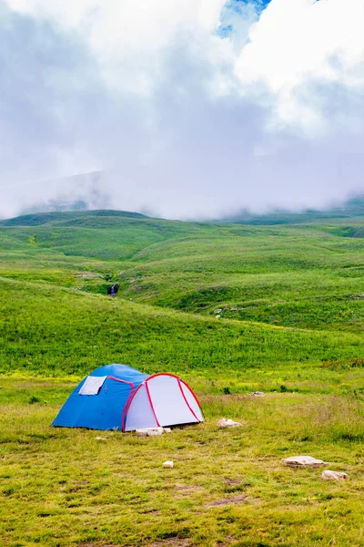 Beautiful green mountain landscape with camping tent in Lago-Naki. Local travel. Green hills with mountain river, blue sky with clouds. Sheer brown rocks.