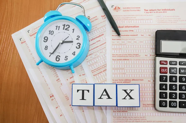 携带计算器 钢笔和蓝色闹钟的澳大利亚税单摆在桌上 从上面看税收概念 立方体税这个词 — 图库照片
