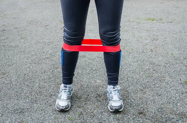 Red elastic for fitness on female legs. Close-up. Train your legs. Training on a sports ground in the yard.