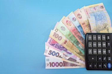 farklı hryvnialar ve hesap makinesinin bir parçası. Mavi arka plan. Tasarruf kavramı. Boşluğun kopyası.