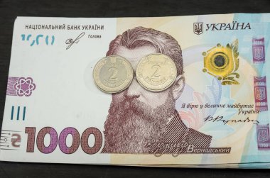 Yüzeysel değeri 2 hryvnia olan iki sikke 1000 hryvnia banknotun üzerinde yatar. Yakın plan. İş konsepti. Vernadsky 'nin kapalı gözleri.