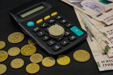 Siyah arka planda 1000 Hryvnia, hesap makinesi ve bozuk para. Yakın plan. İş konsepti. Hesap makinesinde 2 hryvnia değerinde madeni paralar var..