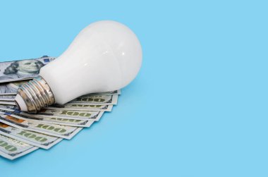 Enerji tasarrufu ampulü ve dolar mavi arka planda. Enerji tasarrufu kavramı. Boşluğun kopyası.