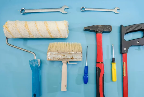 Paint rollers, paint brushes, a hammer and screwdrivers are isolated on blue. The concept of reconstruction and construction.