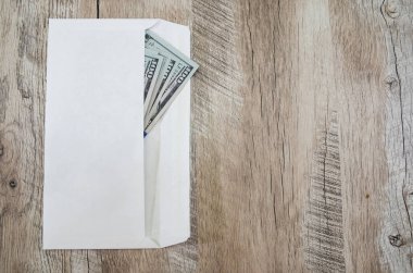 Tahta bir arka planda beyaz bir zarf içinde yüz dolarlık banknotlar. Uzayın kopyası. Mesaj için yer. Yukarıdan görüntüle.