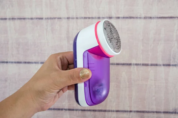 female hand holds a machine to remove pellets from clothes. Wooden background