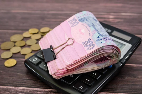 Yuvarlanmış Ukrayna parası hesap makinesinde yatıyor. 200 Hryvnia banknotları ve ahşap arka planda paralar.