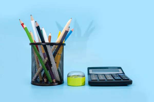 colored pencils and pens in stand and calculator on a blue background.