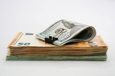 Avro banknotları ve beyaz arkaplanı olan bir yığının üzerinde klipsli 100 dolarlık banknotlar var..