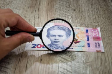 200 Hryvnia 'lık yeni banknot ve bir büyüteç. Ukrayna parası. İş konsepti. Lesya Ukrayna büyüteç / ahşap arka planda.