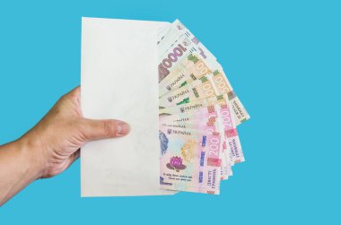 Kadın eli mavi arka planda beyaz bir zarf tutuyor. 200, 500, 1000 hryvnias. Mali konsept.