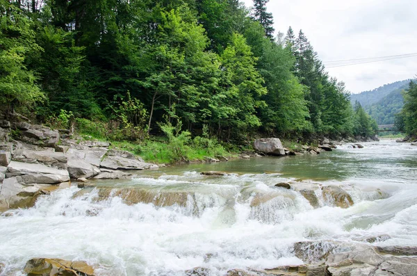 Dağlardaki nehir. Karpatya kırsalının harika bahar manzarası. Orman ve kayalık kıyılar arasında mavi yeşil su. Gökyüzünde bulutlarla güneşli bir gün.