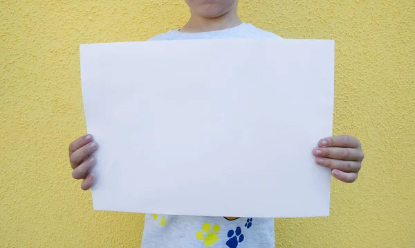 blank white sheet of paper in the hands of a child on a yellow background.