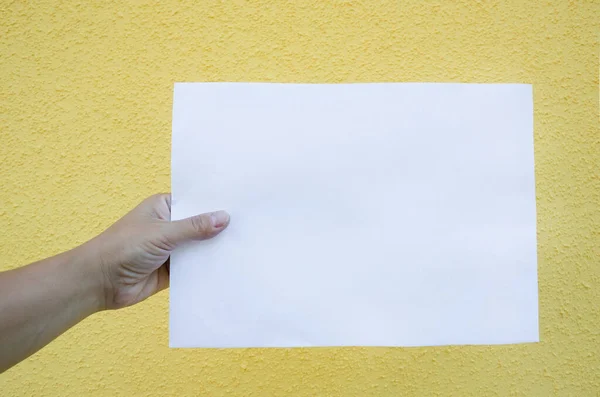 Folha Papel Branca Branco Uma Mão Feminina Sobre Fundo Amarelo — Fotografia de Stock