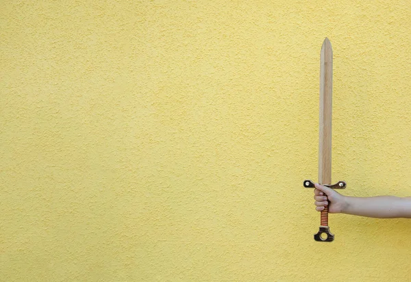 wooden sword in the hand of a child on a yellow background. Copy of space.