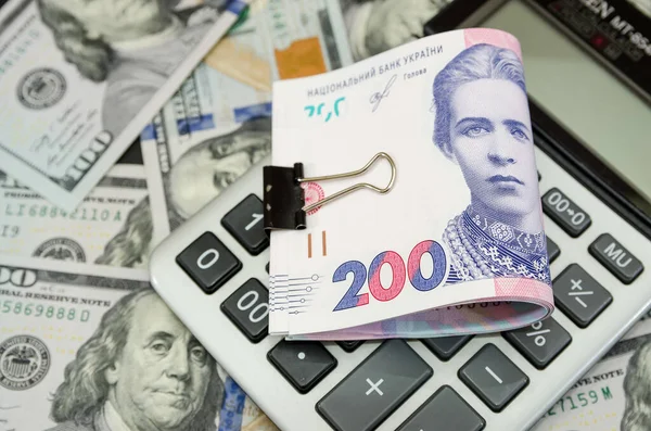 200 Hryvnia 'lık bir kliple sıkıştırıldığında arkaplanda dolarlarla birlikte bir hesap makinesinin üzerinde yatıyor. Yukarıdan görüntüle.