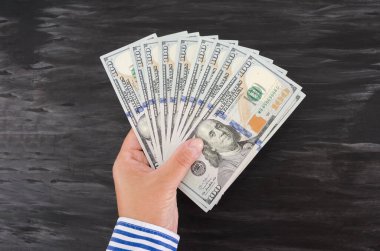 Siyah ahşap bir arka planda kadın eli olan 100 dolarlık banknotlar. Yukarıdan bak. Paralı bir iş kadını eli..