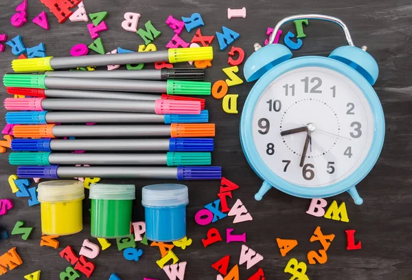 İngiliz renkli harfler, renkli kalemler, kavanoz dolusu guaj ve mavi alarm saati. Okul konsepti. ... okul malzemeleri siyah ahşap arka planda. Yukarıdan bak. Okula geri dön..