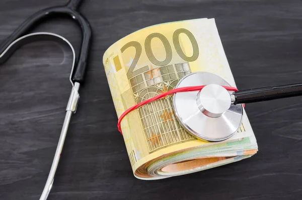 euro banknotes and medical stethoscope on a dark wooden background.