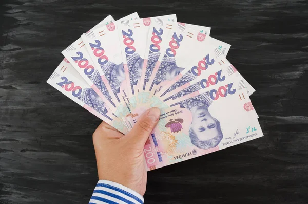 İş kadınının elinde 200 Hryvnia 'nın banknotları var. Siyah ahşap arka plan. Mali konsept.