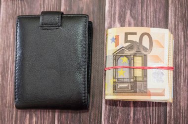 Siyah adamın cüzdanı ve 50 avroluk banknotlar. Ahşap bir masada elastik bir bantla bağlanmış. Çok para. İş konsepti. Yukarıdan görüntüle.