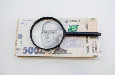 Bir yığın Hryvnia banknotları ve bir büyüteç. Hafif arkaplan. Bir sürü para. Ukrayna Hryvnia 'sı. Yukarıdan görüntüle.
