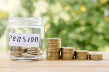 Üzerinde PENSION yazan cam kavanoz ve ahşap masa üzerinde madeni paralar. Metin için boşluk