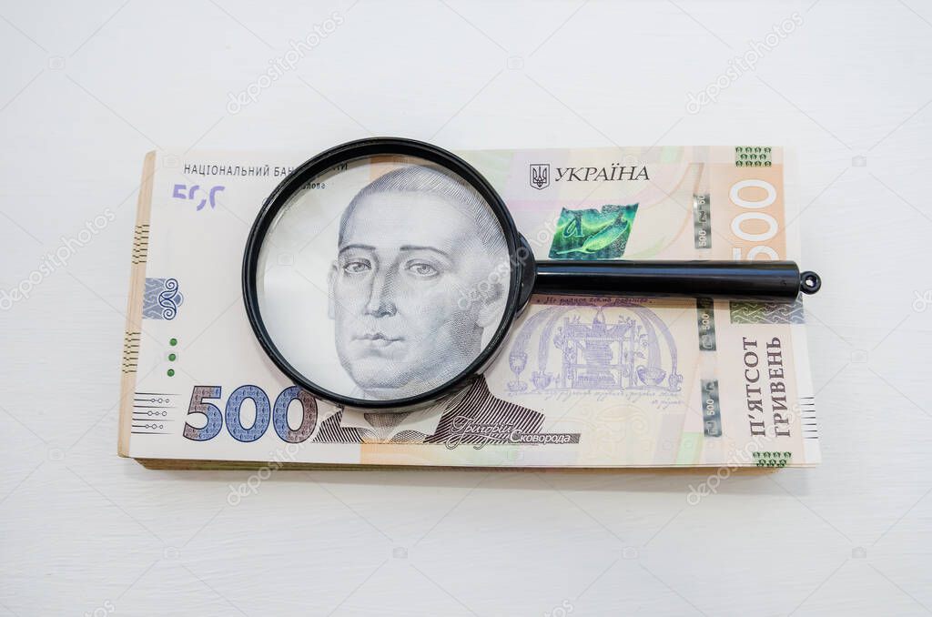 Stack of hryvnia banknotes and a magnifying glass. Light background. A lot of money. Ukrainian hryvnia. View from above.