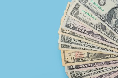 mavi arka planda bir vantilatörün içine katlanmış farklı dolarlar. Finansal konsept. Boşluğun kopyası.