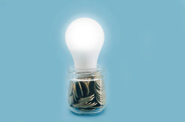 コインの瓶と照明付きの省エネ電球です 青の背景 節電コンセプト — ストック写真