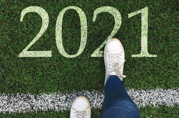 Happy New Year 2021. Women\'s feet cross the white line and step on 2021.Top view of white sneakers on asphalt road with text 2021, new year celebration concept