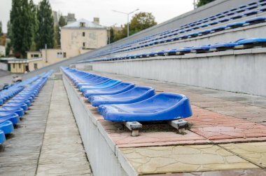 Stadyumda bir sürü boş koltuk var. Mavi sandalyelerin dokusu. Plastik koltuklar sıraya dizildi. Kirli ve tırmalanmış fan koltukları. Yağmurdan sonra tadium